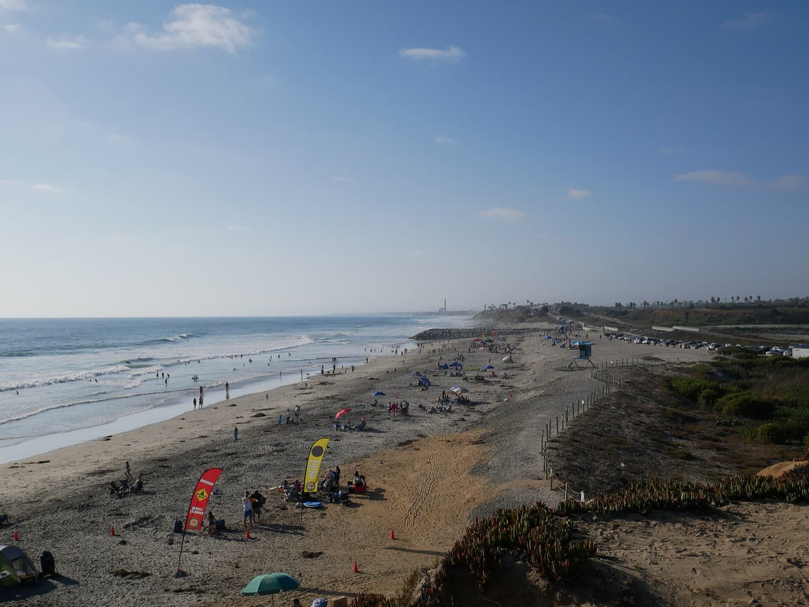 South Carlsbad State Beach seen from the bluff, with surf on the left, beachgoers on the sand and a lifeguard tower in the distance.
