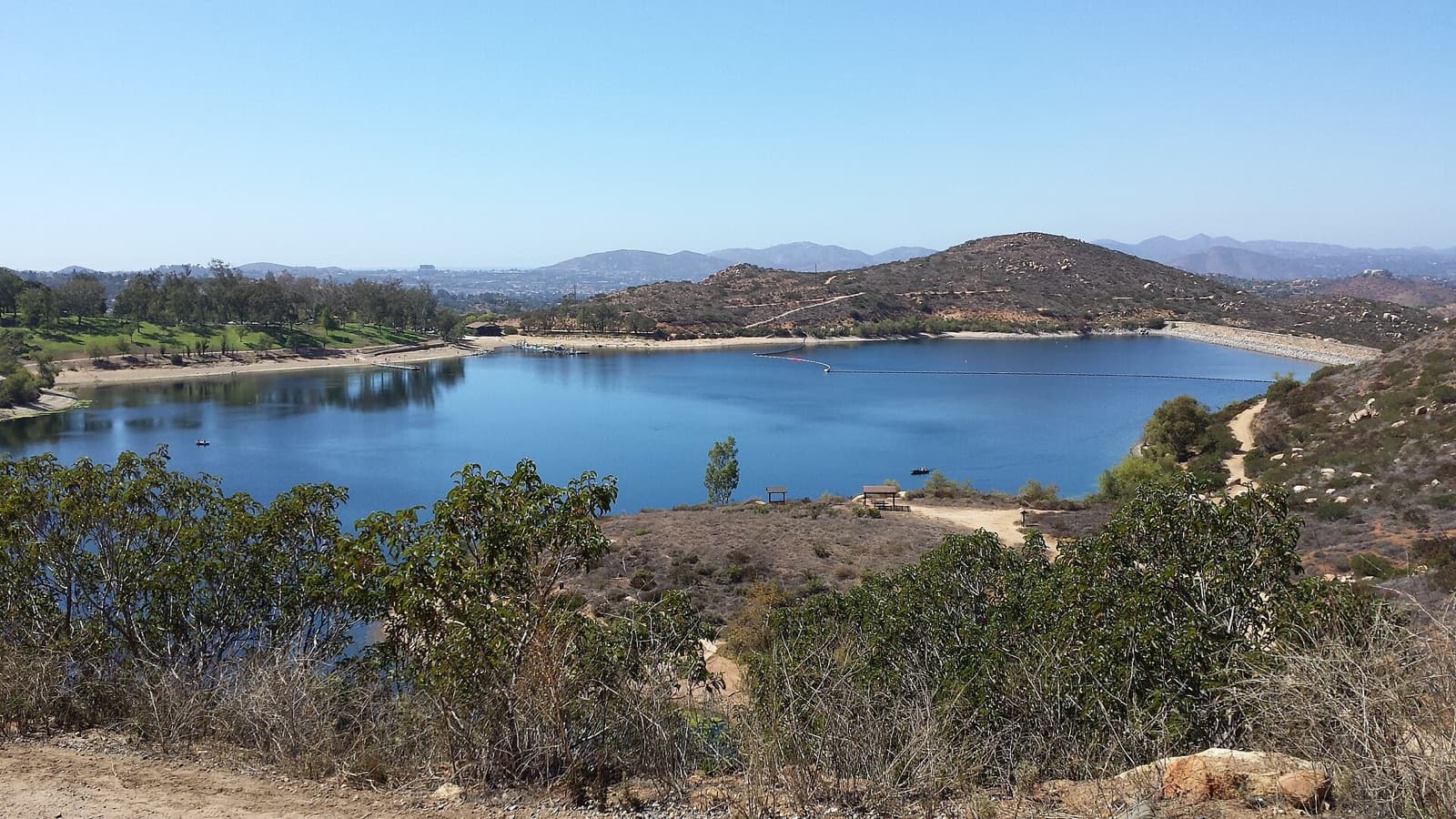 Lake Poway with its boat marina and surrounding hills under a clear sky, viewed from the Mount Woodson trail.